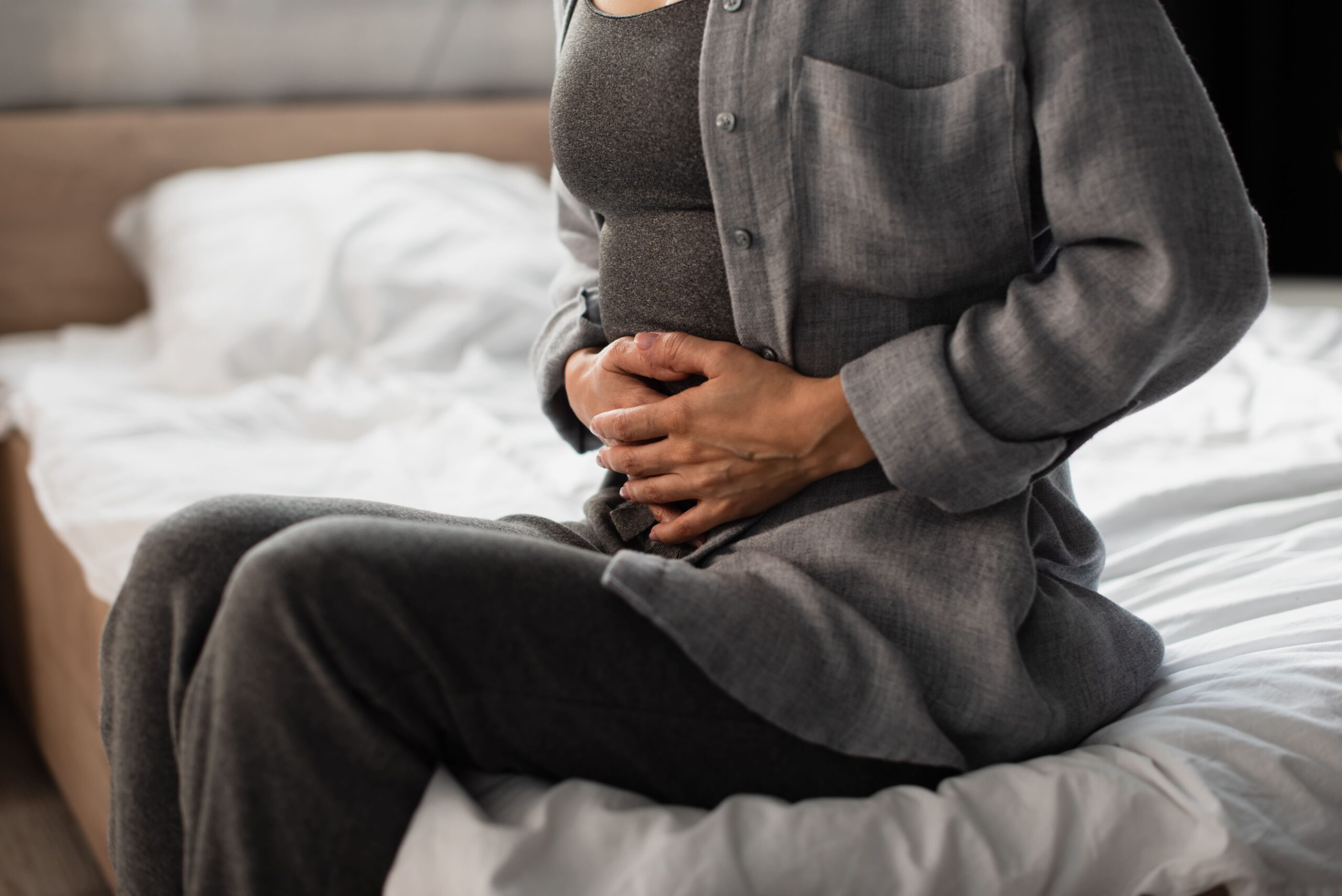 An adult sitting quietly on the edge of a bed holding their abdomen, reflecting the complex and persistent nature of IBS symptoms beyond simple dietary triggers