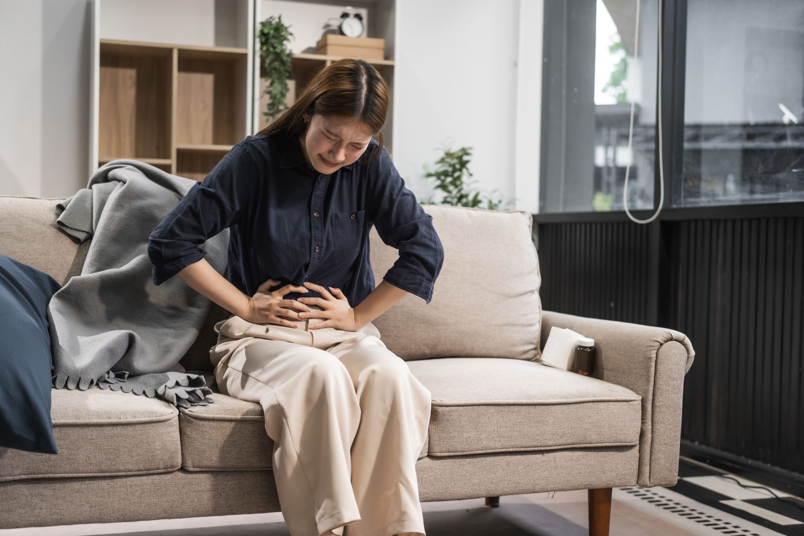 A person sitting on a couch with a hand on their abdomen, looking overwhelmed, showing how stress and internal state can trigger IBS symptoms as much as food